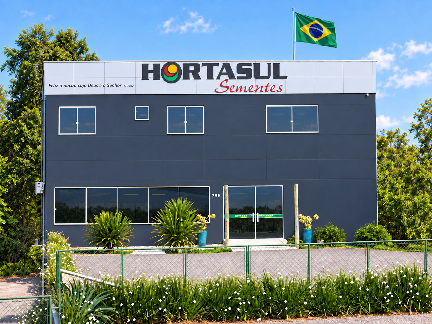 Fachada da Hortasul Sementes com bandeira do Brasil acima do prédio e versículo em itálico no canto superior esquerdo